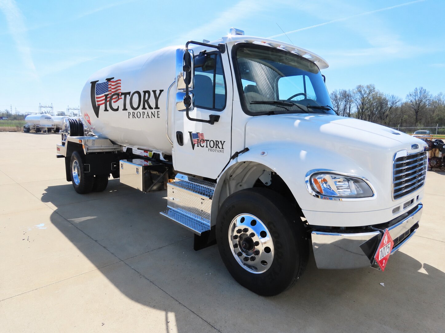 Front passenger-side view of a Victory Propane Freightliner bobtail truck parked on a concrete lot, with a second propane truck in the background.