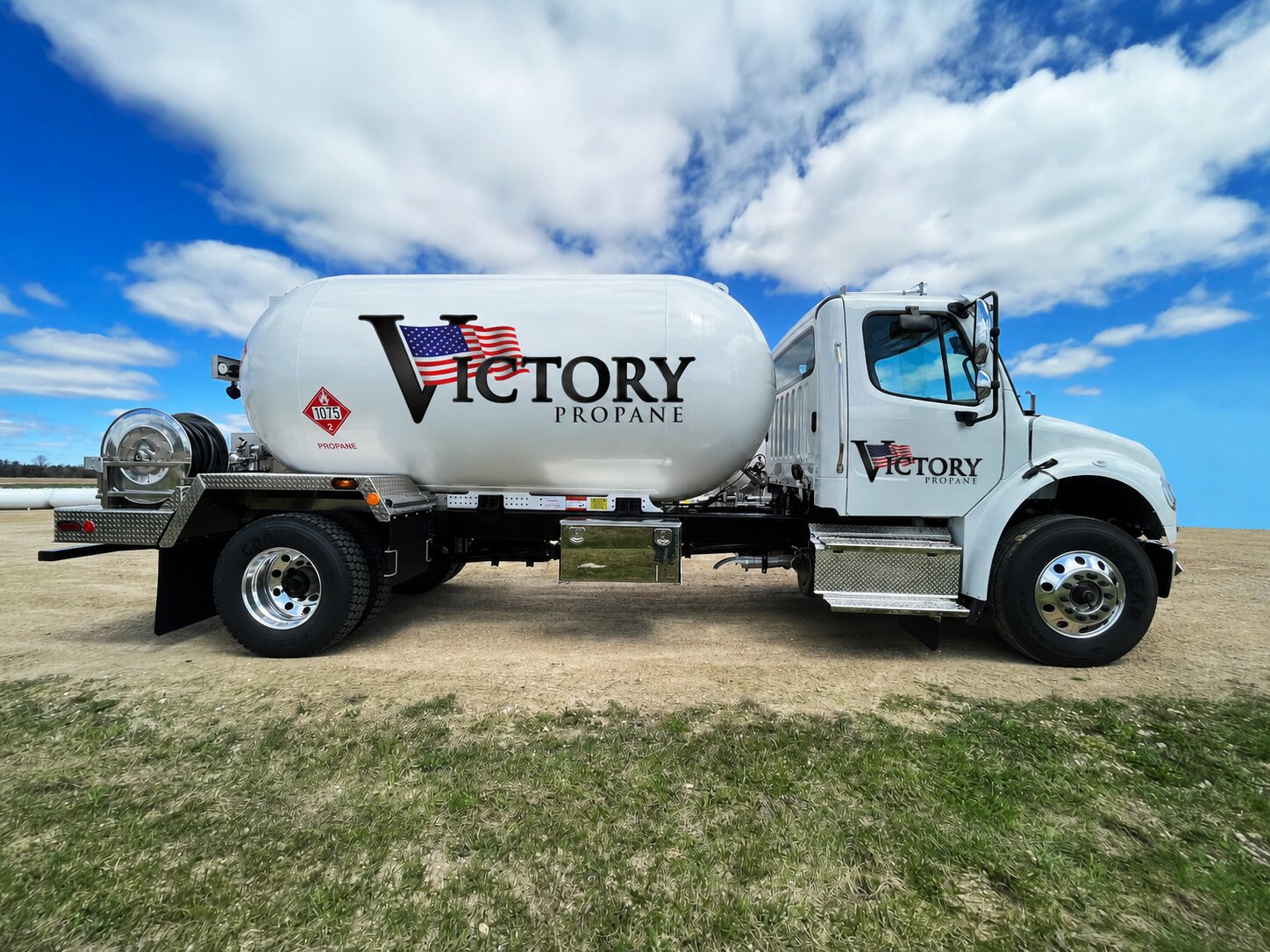 Full driver-side profile of a Victory Propane bobtail truck parked in a field under a blue cloudy sky.